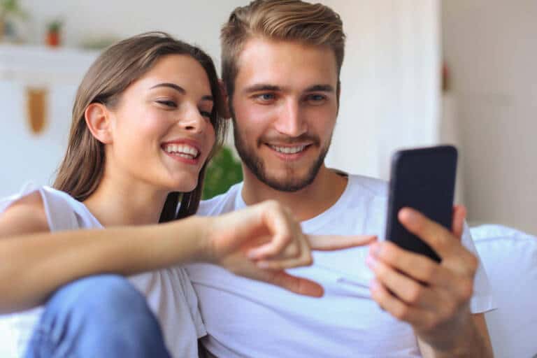 young couple watching online content smart phone sitting sofa home living room